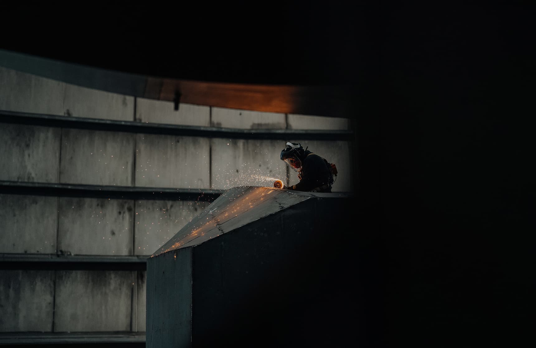 A worker fabricating a large electric vessel hull, sparks flying, inside Arc's factory.