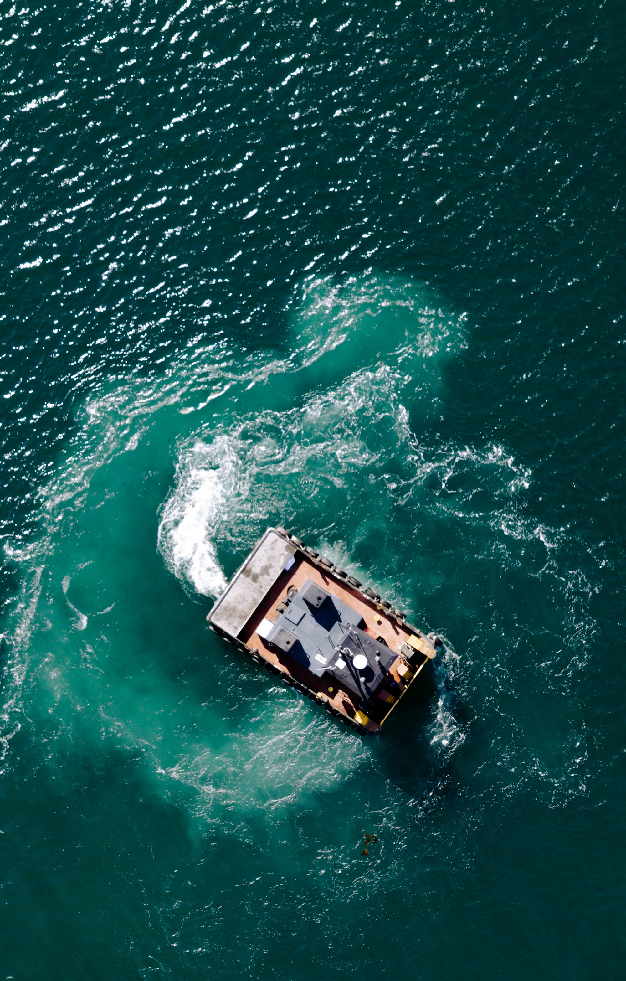 An aerial photograph of a work boat turning in the water.