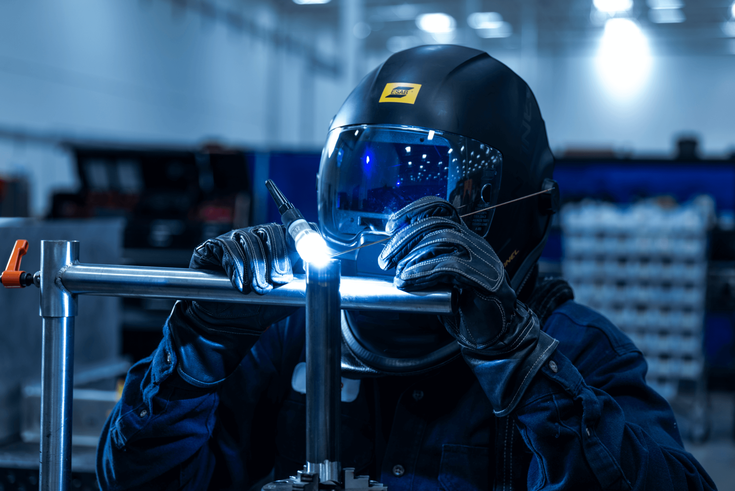 A photograph of a man in a helmet welding two pipes together..