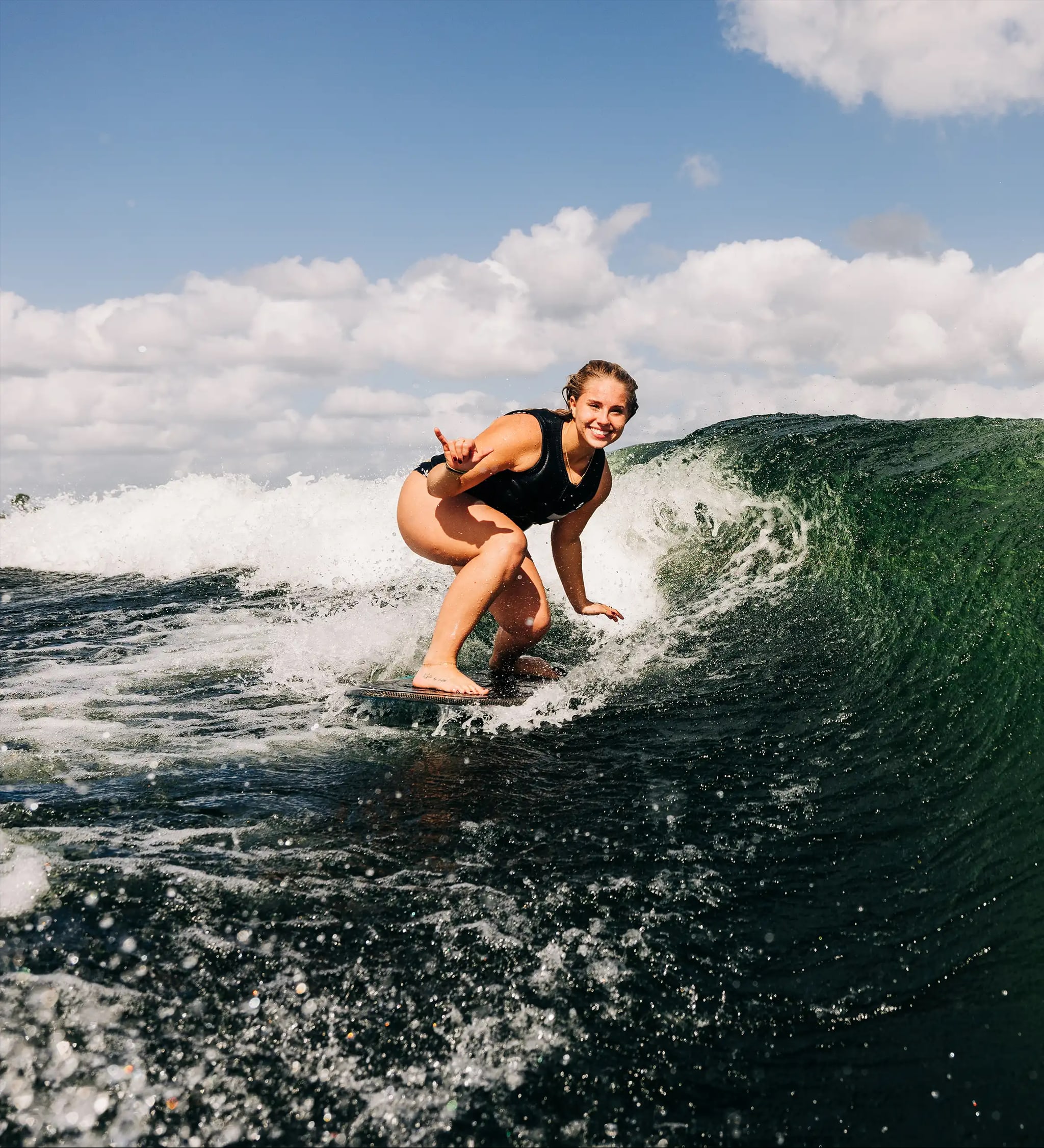 A photograph of a woman surfing toward the camera.