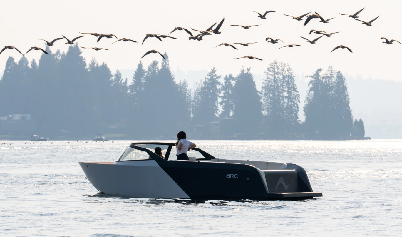 A rear port-side view of the Arc One on a lake beneath a flock of birds