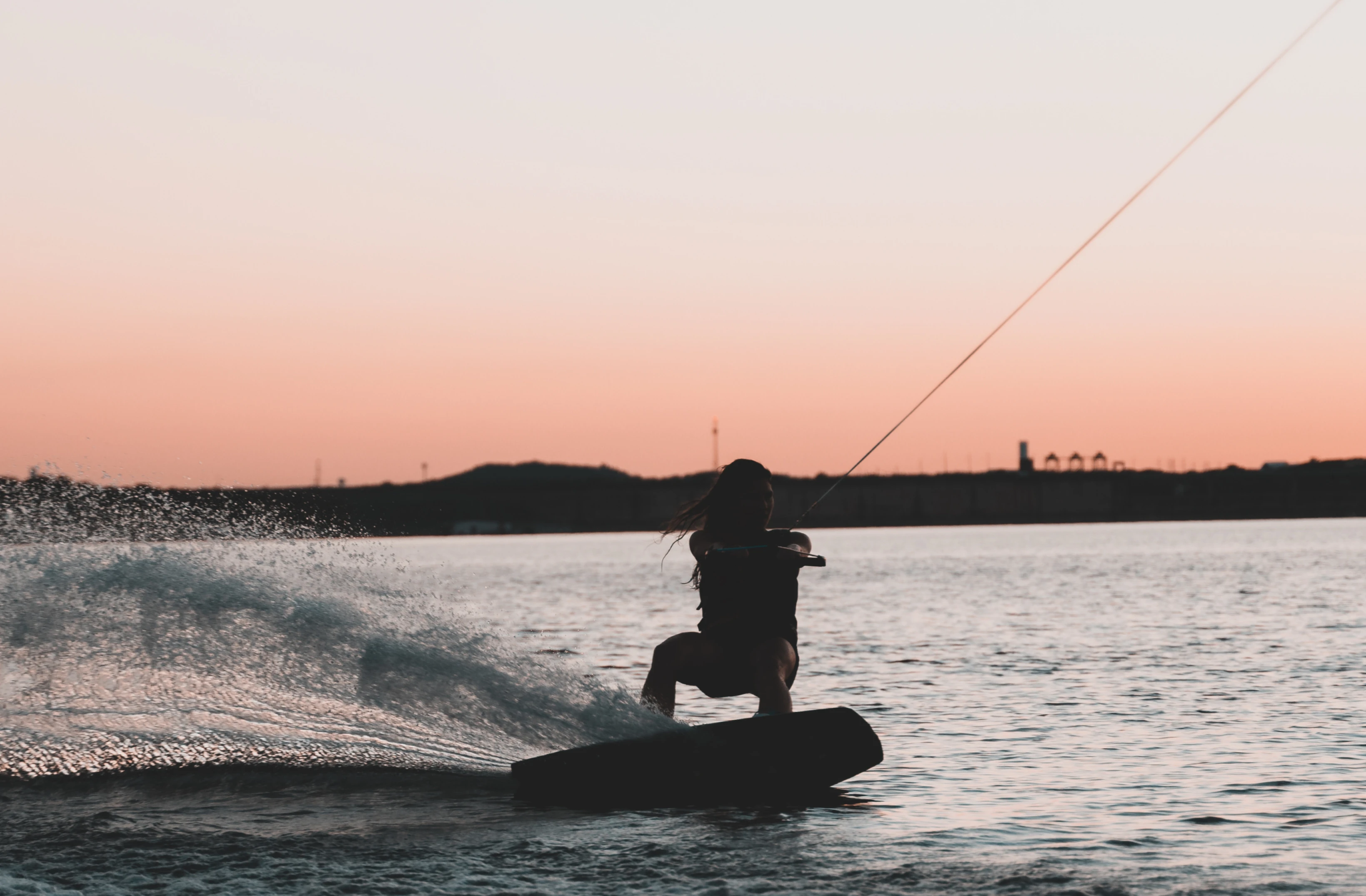 The silhouette of a wake surfer in front of a peach-colored sunset